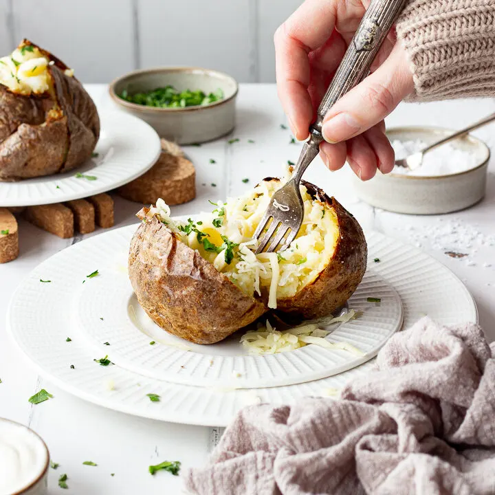 Someone forking a Ninja air fryer jacket potato with cheese on a white plate