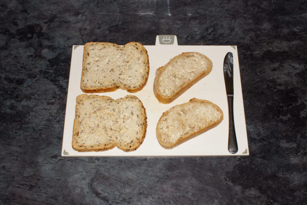 Buttered bread on a chopping board with a knife