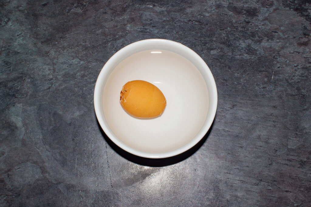 A cracked air fried egg in a bowl of cold water