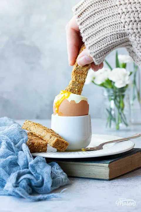 Someone dunking toast into an air fryer boiled egg