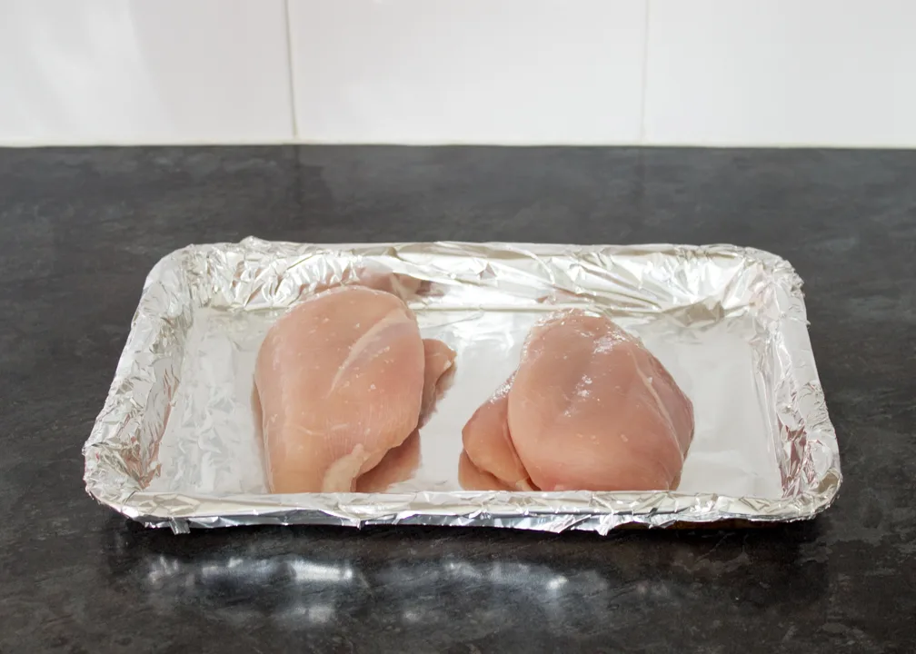 Two chicken breasts on a foil lined baking tray