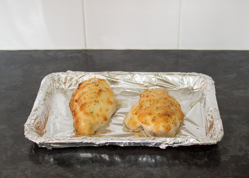 Two baked parmesan chicken breasts on a tray