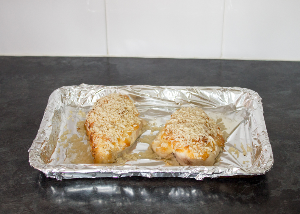 Two cheese topped chicken breasts on a tray with panko breadcrumbs
