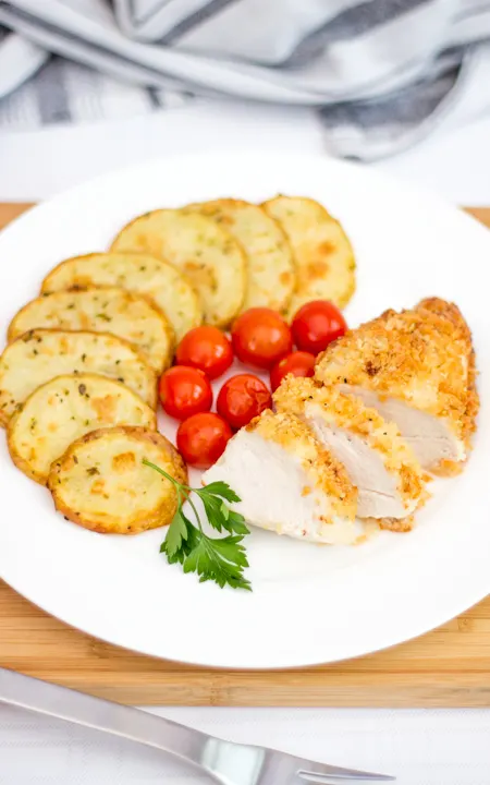 Baked parmesan chicken on a plate with potato thins and tomatoes