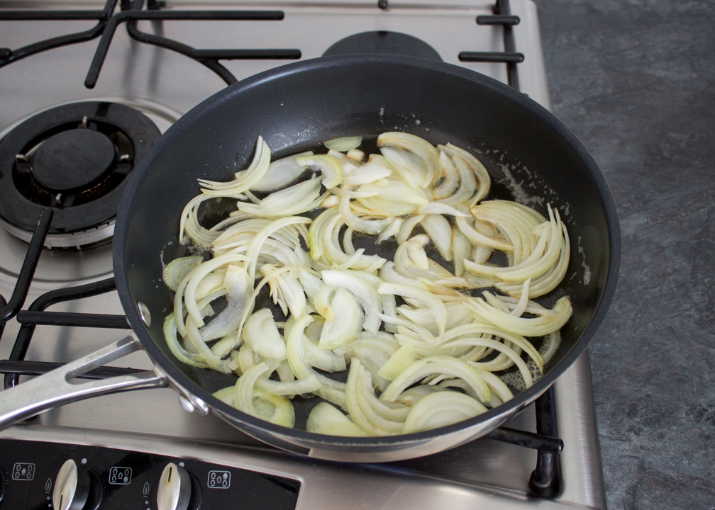 Thinly sliced onions in a large frying pan
