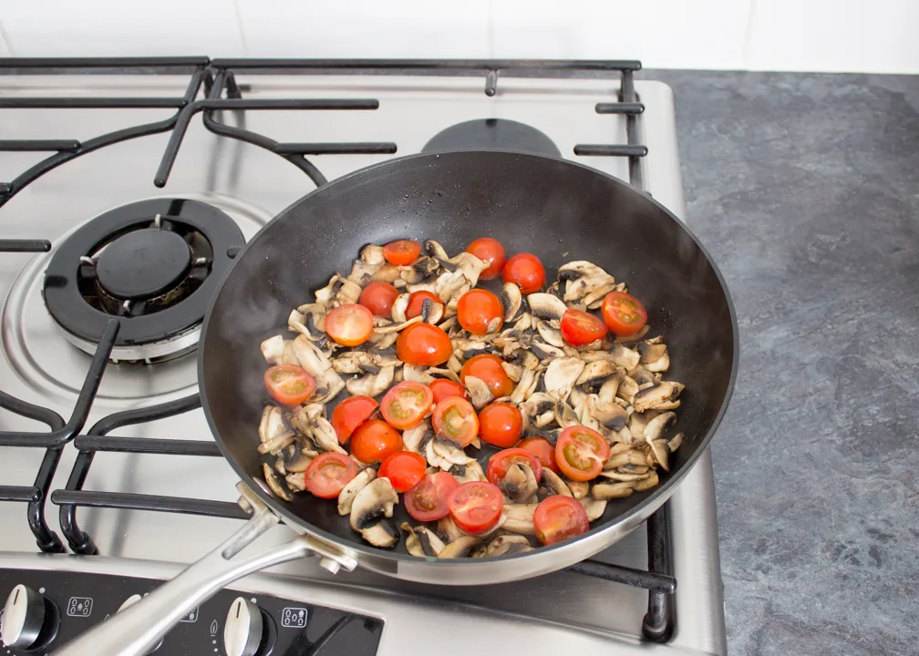 Sliced mushrooms and halved cherry tomatoes frying in a pan