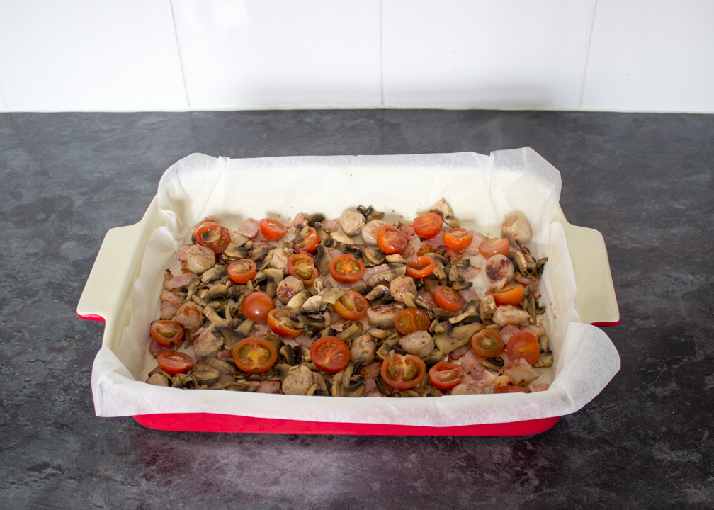 Sausage, bacon, mushrooms and tomatoes in a lined ovenproof dish