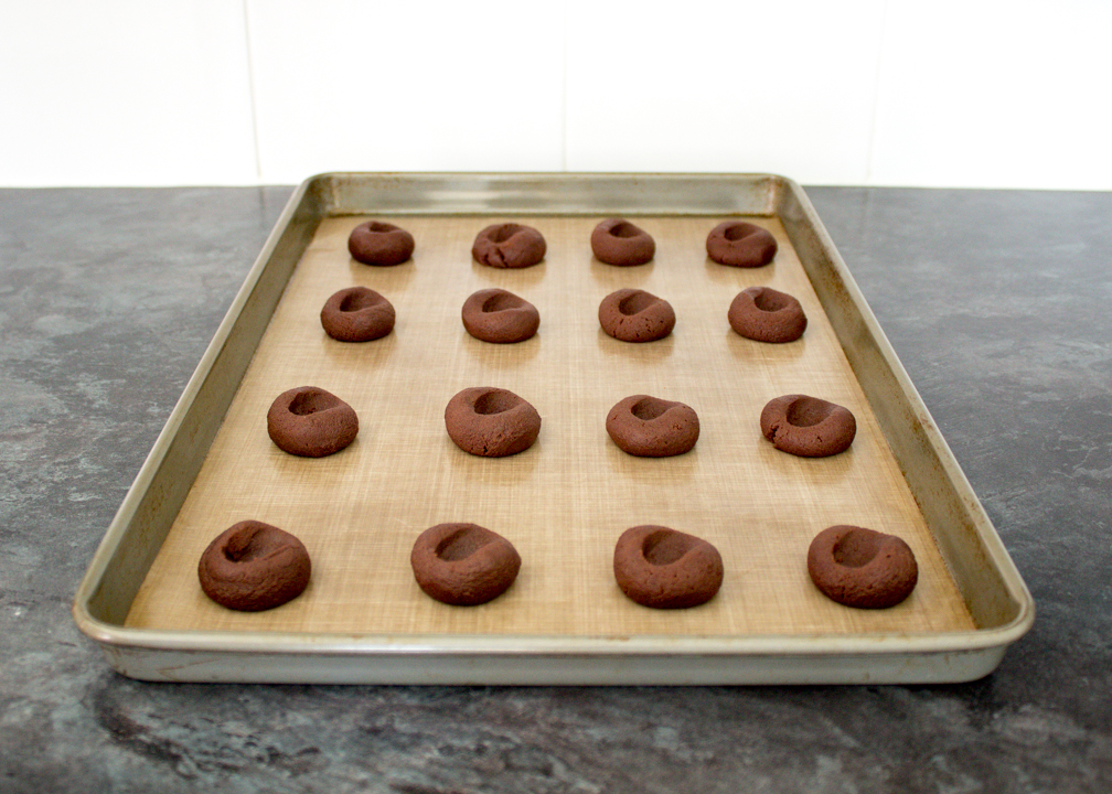 Chocolate cookies with thumbprint indents on a baking sheet