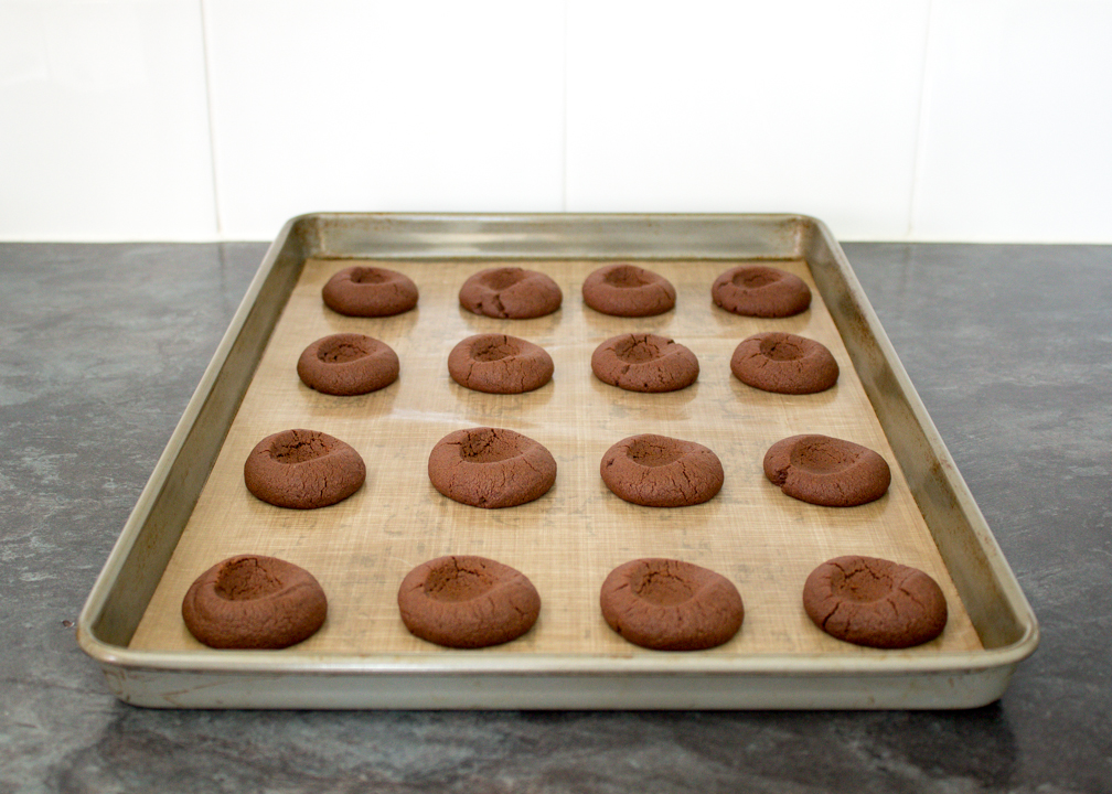 Baked chocolate thumbprint cookies on a baking sheet