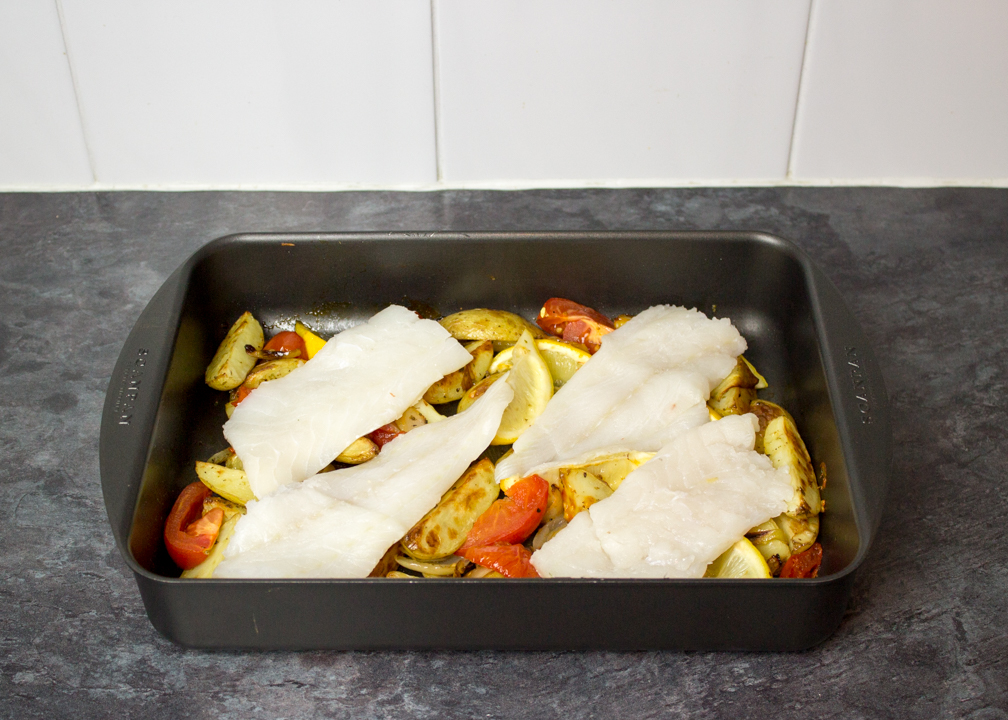 Partially cooked potato wedges and raw fish in a roasting pan