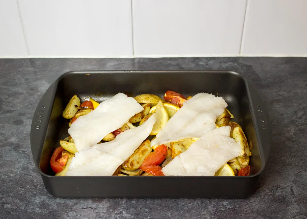Partially cooked potato wedges and raw fish in a roasting pan