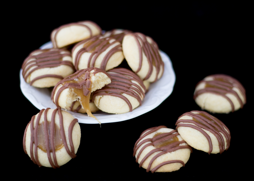 Twix thumbprint cookies in a white plate with caramel oozing out