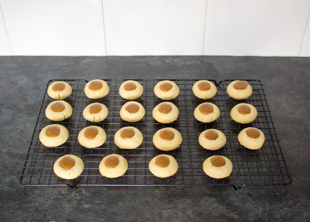 Thumbprint cookies filled with caramel on a wire rack