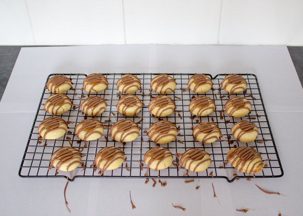 Twix thumbprint cookies with drizzled chocolate on a wire rack