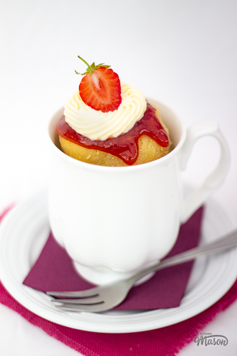 Vanilla mug cake in a white mug topped with strawberries and sweetened cream