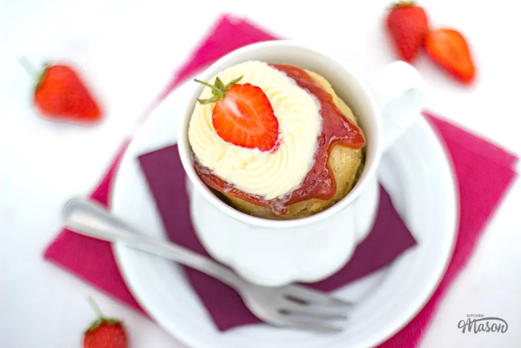 A vanilla mug cake with strawberries and cream on a plate with a fork