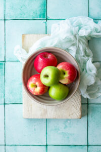 A bowl of red and green apples on a wooden board