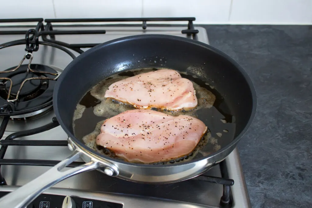 Two chicken breasts frying in a saucepan