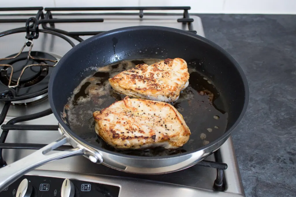 Two cooked chicken breasts in a frying pan
