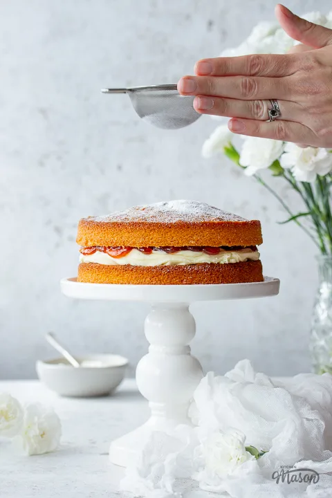 Icing sugar being dusted over an air fryer sponge cake