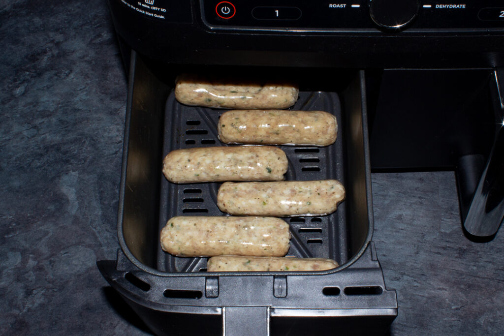 6 raw sausages in an air fryer drawer