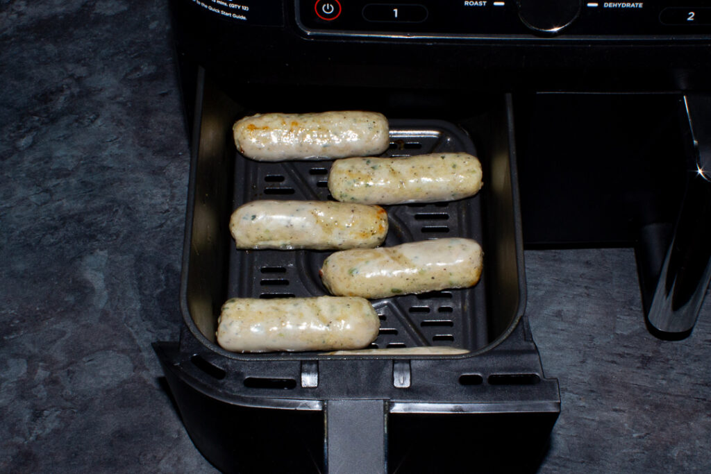 6 partially cooked sausages in an air fryer drawer