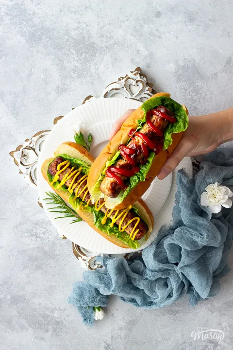 Someone holding an air fryer sausage in a finger bun with ketchup and lettuce