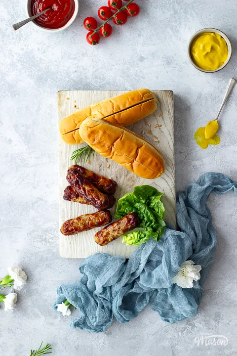 Air fried sausages on a chopping board with finger buns and lettuce