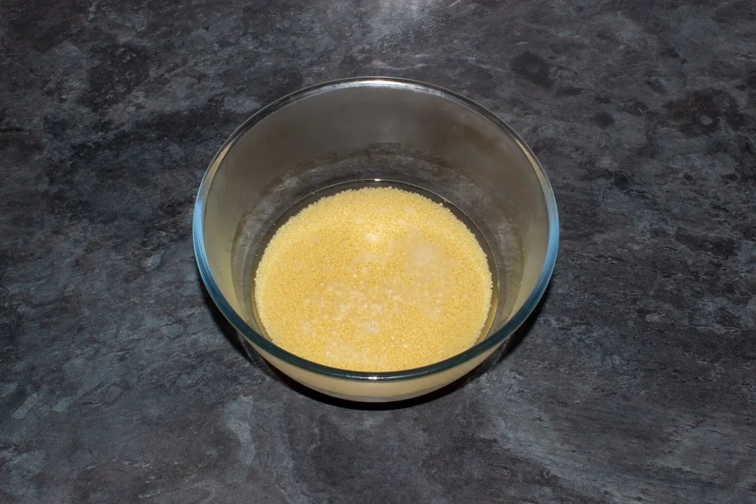 A glass bowl with boiling water and couscous in it