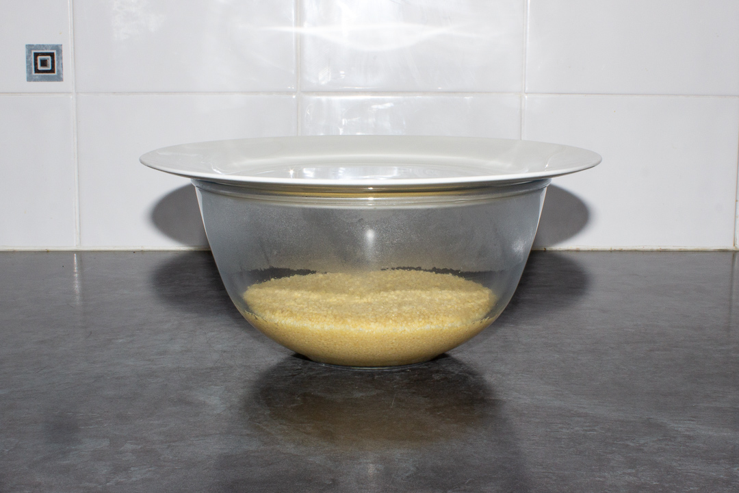 A bowl with boiling water and couscous in it, with a plate on top