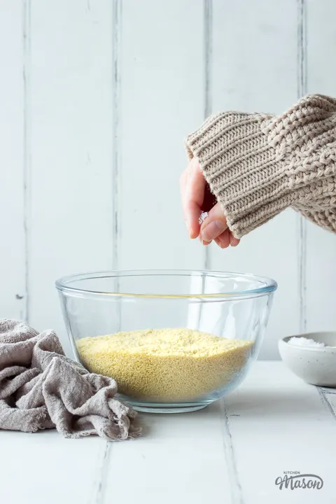 Front view of someone salting couscous in a glass bowl