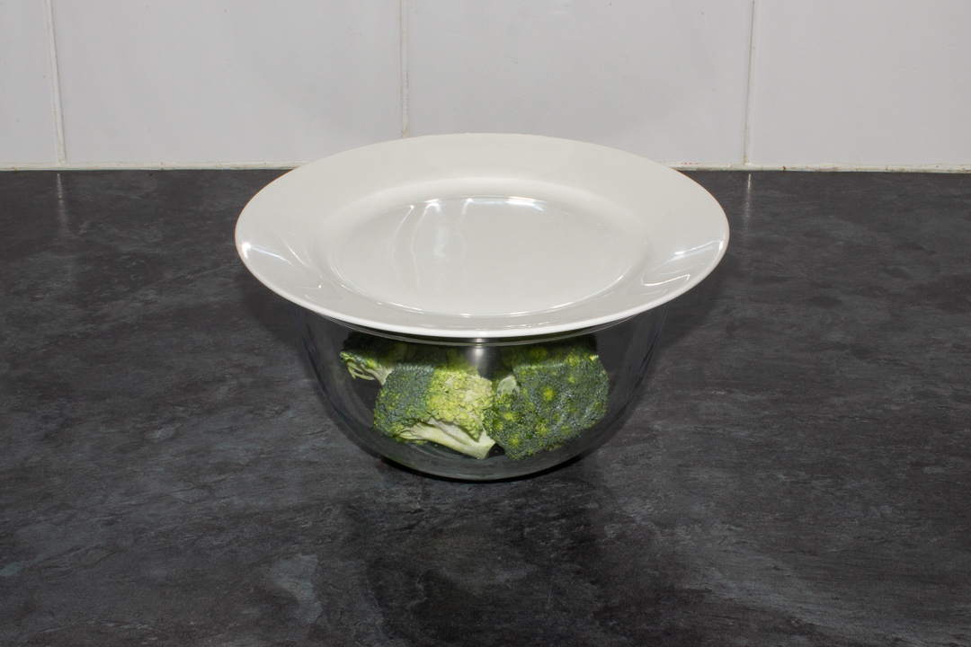 Raw broccoli and water in a bowl with a plate on top