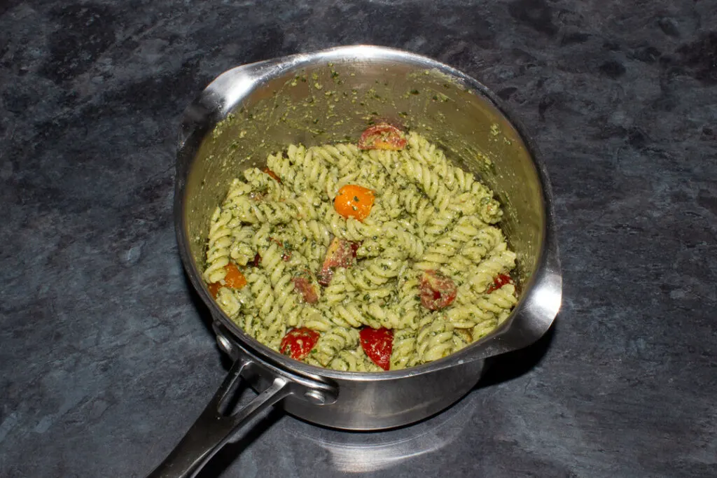 Cooked pasta, cherry tomatoes and pesto mixed together in a saucepan
