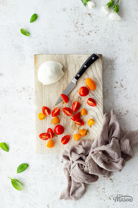 Tomatoes and mozzarella being chopped on a wooden board