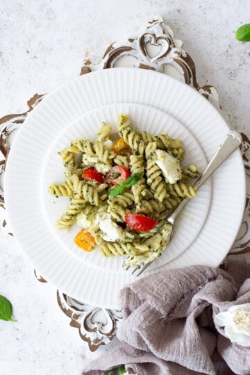 A plate of mozzarella pesto pasta and tomatoes on a white board