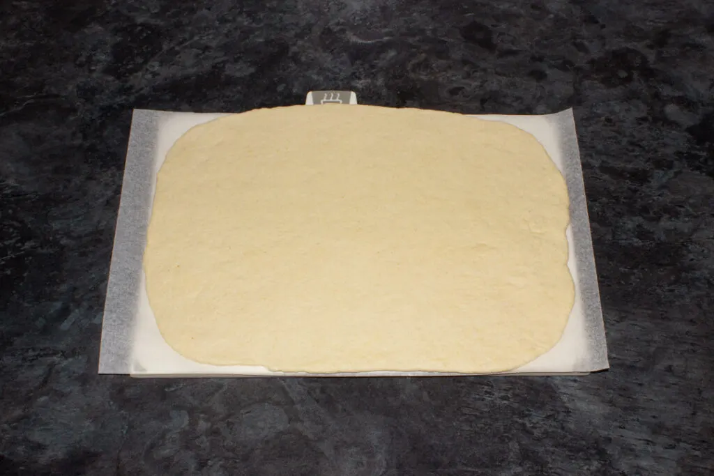 Rolled out pizza dough on baking paper
