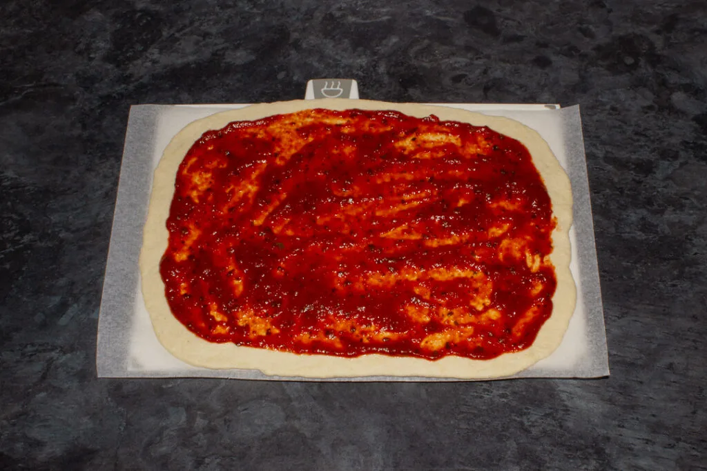 Pizza dough with tomato sauce spread over it