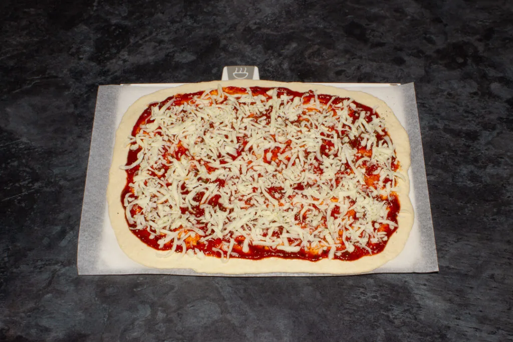 An unbaked pizza on baking paper, ready for the oven