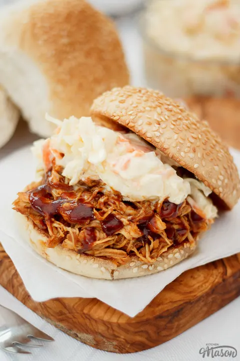 A bun filled with slow cooker bbq chicken and coleslaw on a chopping board