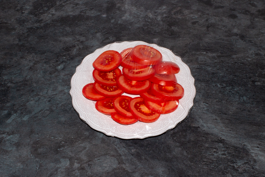 Sliced tomatoes on a plate covered in cling film