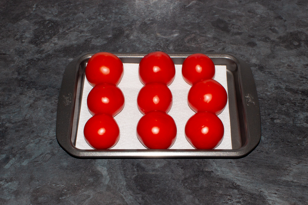 Whole tomatoes on a baking tray lined with kitchen roll
