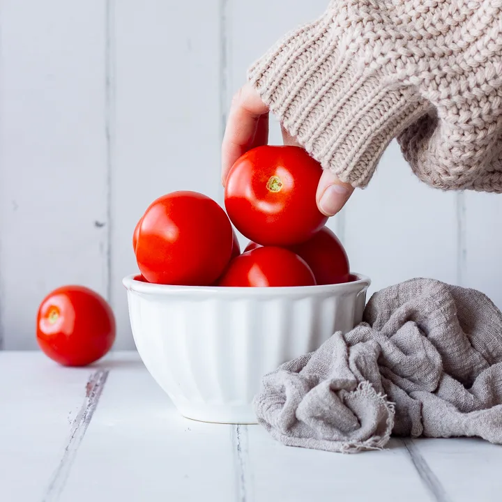 Someone taking a tomato from a bowl
