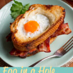 An egg in a hole bacon sandwich on a green plate with a fork