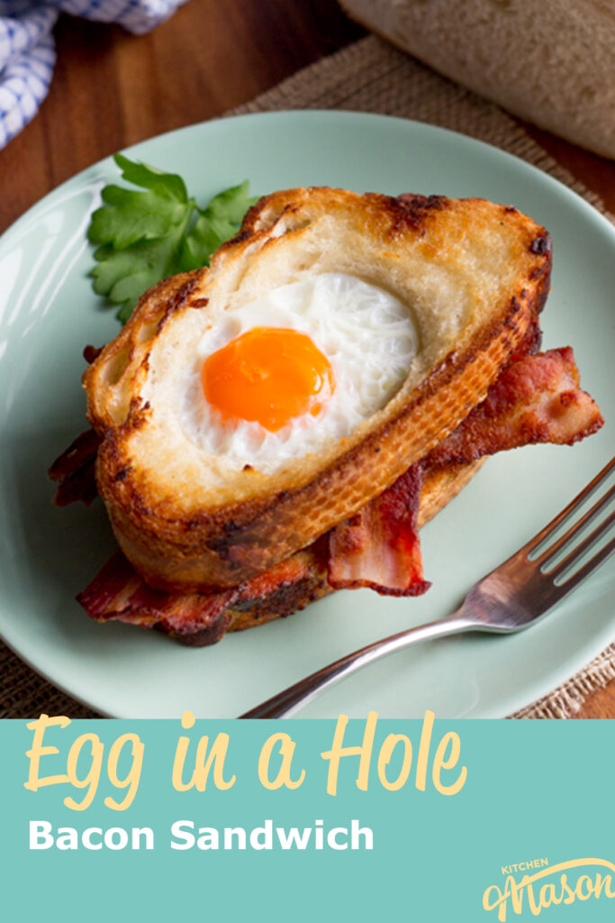 An egg in a hole bacon sandwich on a green plate with a fork