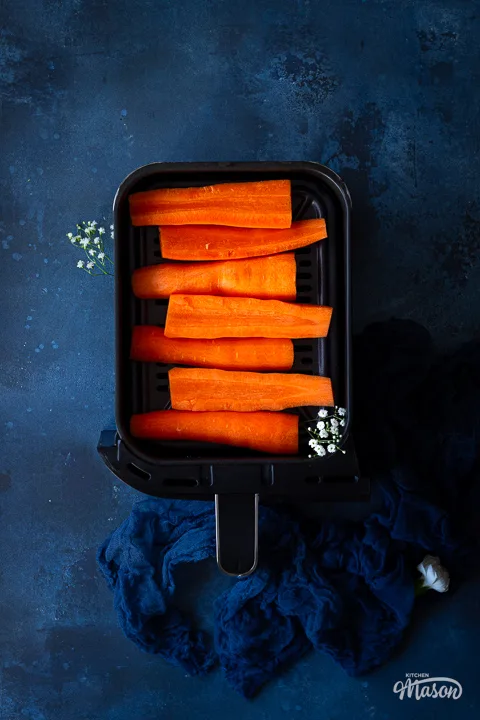 Raw carrot halves in an air fryer drawer with a napkin