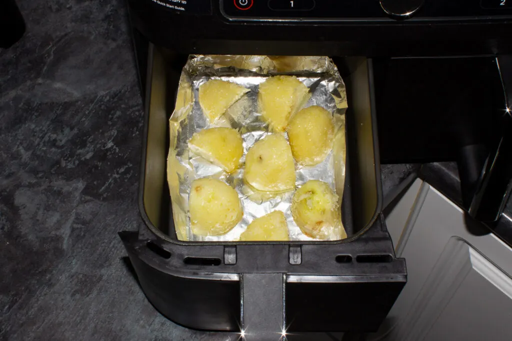 Part cooked potatoes in a foil tray in an air fryer