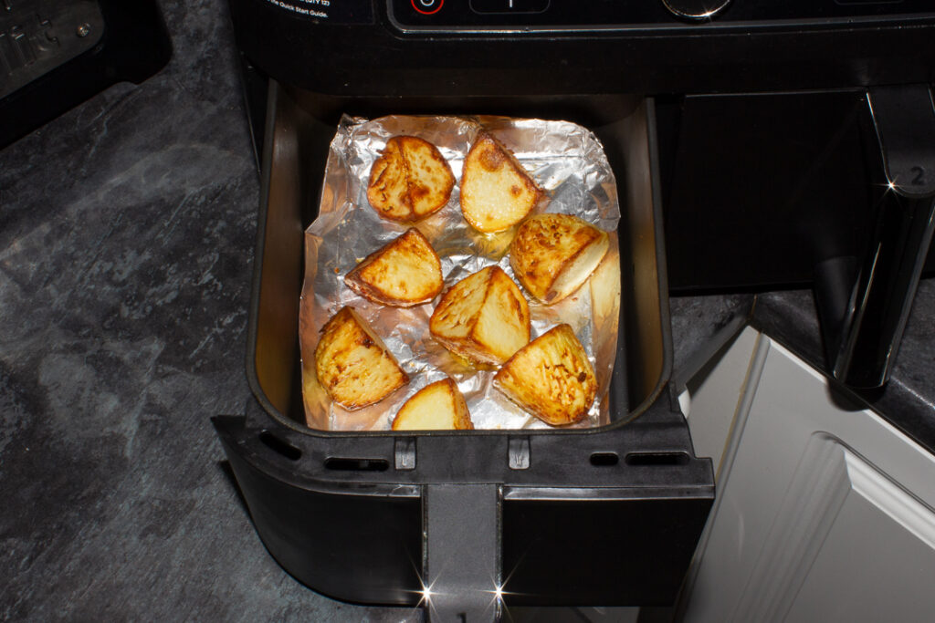 Two thirds cooked roast potatoes in a tin foil tray in an air fryer drawer