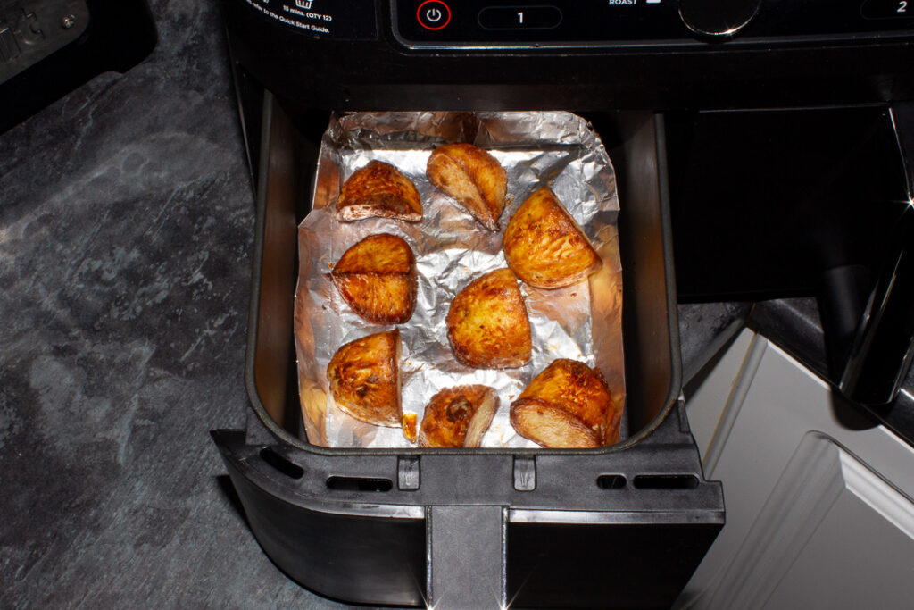 Fully cooked roast potatoes in a tin foil tray in an air fryer drawer