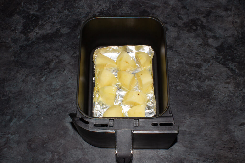 potatoes in a tin foil tray in an air fryer drawer