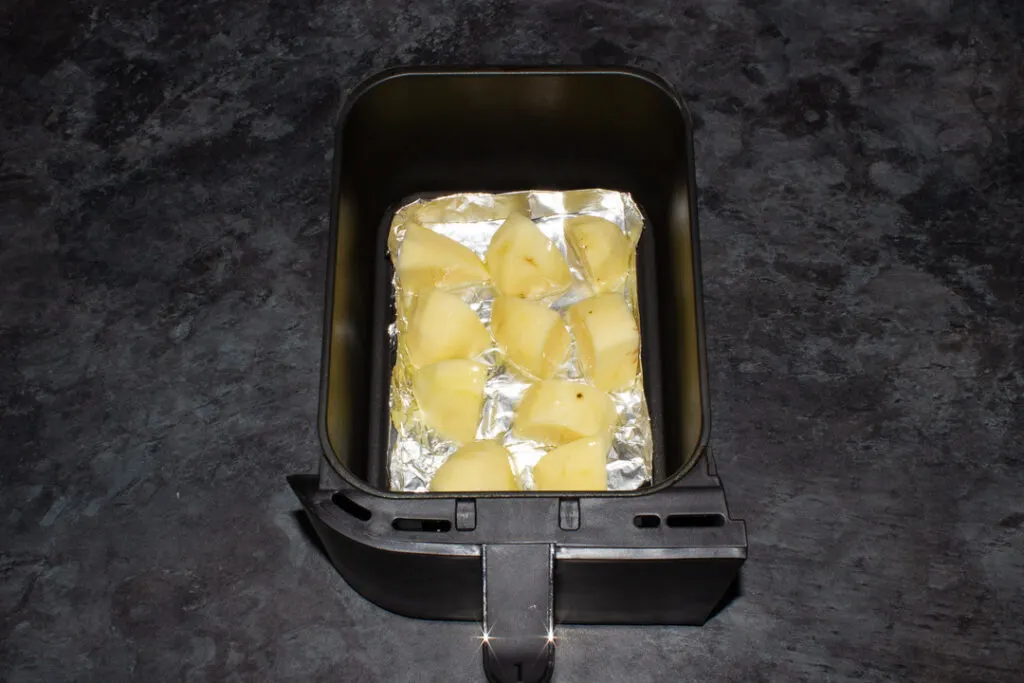 potatoes in a tin foil tray in an air fryer drawer